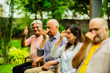 Indian seniors doing Pranayama in group while seated outdoors in garden with closed eyes