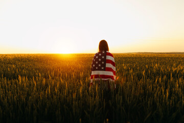 Young woman with American flag in a wheat field at sunset. 4th of July. Patriotic holiday, american...