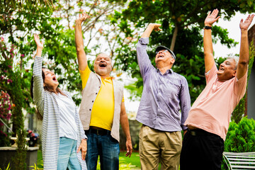 Seniors doing group huddle cheer standing outdoors in garden with happy and positive expressions