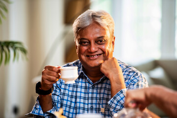 Elderly Indian man enjoys morning tea at home with smile while seated at elegant dining space