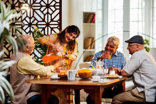 Seniors serving and eating together during happy indoor reunion around modern Indian dining table