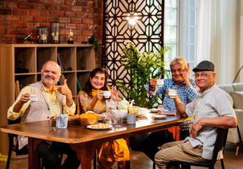 Seniors serving and eating together during happy indoor reunion around modern Indian dining table