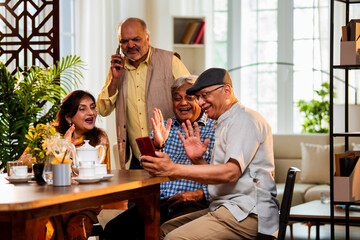 Seniors video calling at dining table during happy indoor meal with friends and warm conversation