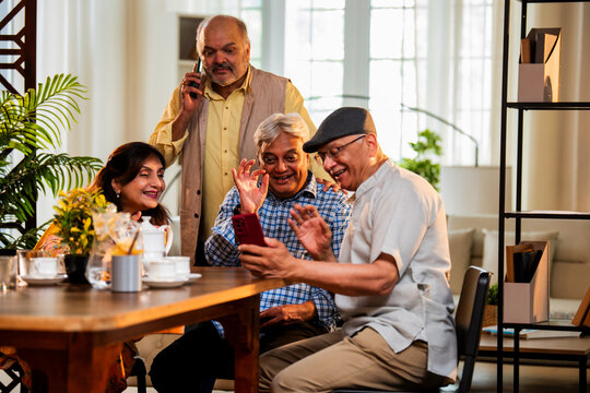 Seniors video calling at dining table during happy indoor meal with friends and warm conversation