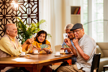 Indian senior citizens playing card game and bonding at cozy home dining table during reunion
