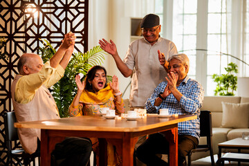 Indian senior adults playing jenga game and bonding while seated together at indoor dining table