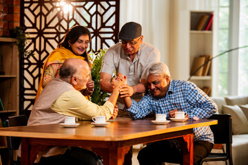 Elderly Indian men arm wrestling while women cheer during fun indoor game at retirement reunion