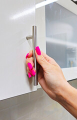 Woman's hand with manicure opens kitchen cabinet
