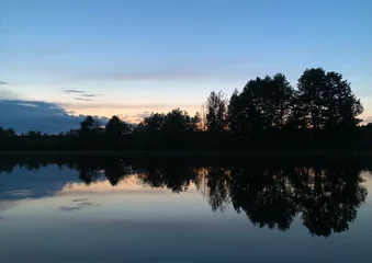 Beautiful twilight sunset. The dark dense summer forest is reflected in the mirrored lake. Bright blue sky, with the last red rays of the sun. Nature is amazing. Wallpaper, postcard, design,