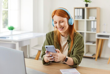 Happy woman freelancer working online from home office, using a laptop and phone. Engaging in...