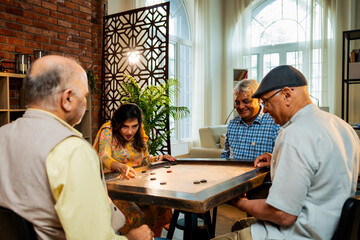 Indian retired adults playing carrom board game at dining table in cheerful indoor group activity