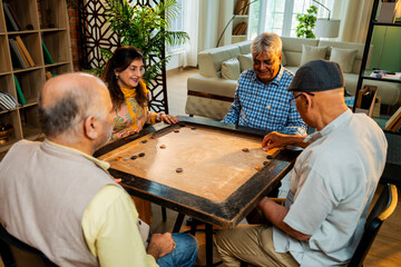 Indian retired adults playing carrom board game at dining table in cheerful indoor group activity