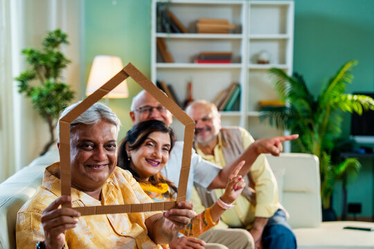Senior friends holding home cutout to convey old age housing support and retirement care message