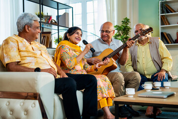 Senior group performing music indoors with guitar during joyful reunion on sofa at modern home