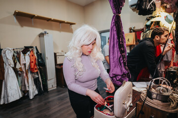 The scene depicts performers organizing their costumes and applying makeup backstage, showcasing...