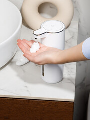 Woman using white automatic soap dispenser in bathroom
