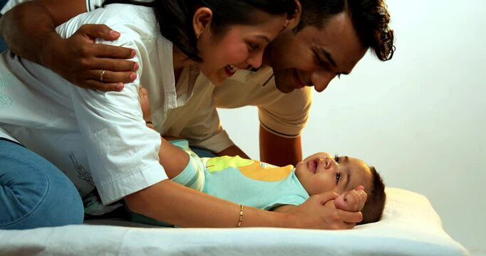 Parents playing with baby boy while lying on white bed in cozy home setting, side view angle showing joyful bonding, affection, parenting moments, love for newborn in Indian modern family lifestyle