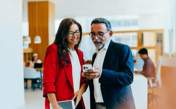 Two senior professionals discussing a topic on a mobile phone inside an office