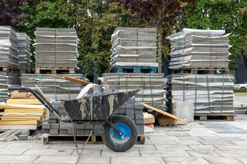 Stacks of paving slabs and a dirty wheelbarrow at urban construction site