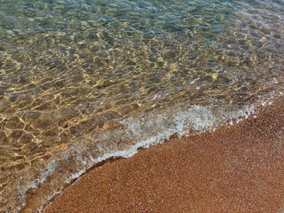 Clear sea soft waves on pinkish sand beach 