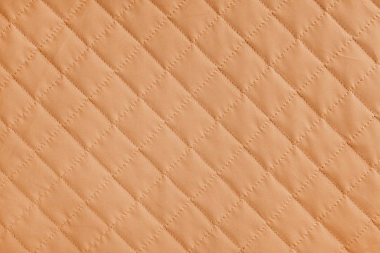 Checkered, diamond stitching pattern, orange quilted fabric background. Blanket or puffer jacket, stitch rhombus texture close up, macro. Wallpaper, backdrop.