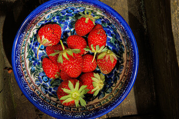 A colorful bowl of freshly picked strawberries in a wooden box, representing a homegrown harvest.