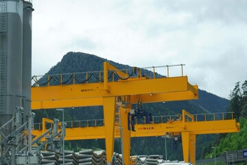 Yellow gantry cranes at a railway construction site with mountains in the background