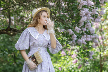A beautiful young blonde woman, against a background of blooming lilacs, in a lilac vintage dress. A walk in the park.
