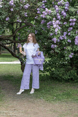 A beautiful young blonde woman, against a background of blooming lilacs, in a lilac trouser suit. Femininity and nature.