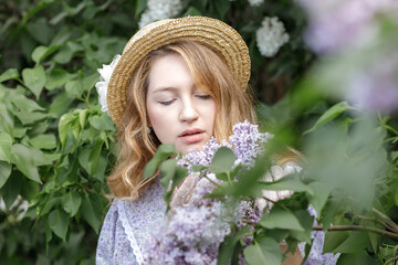 A beautiful young blonde woman, against a background of blooming lilacs, in a lilac vintage dress. A walk in the park.