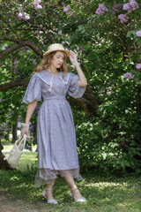 A beautiful young blonde woman, against a background of blooming lilacs, in a lilac vintage dress. A walk in the park.