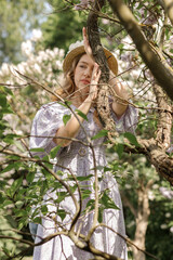 A beautiful young blonde woman, against a background of blooming lilacs, in a lilac vintage dress. A walk in the park.