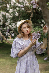 A beautiful young blonde woman, against a background of blooming lilacs, in a lilac vintage dress. A walk in the park.