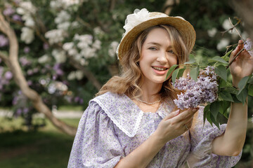 A beautiful young blonde woman, against a background of blooming lilacs, in a lilac vintage dress....