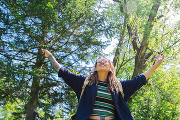 Woman Stands in a Forest, Her Arms Raised Up. Sunlight Filters Through the Trees, Creating a Vibrant, Natural Atmosphere.