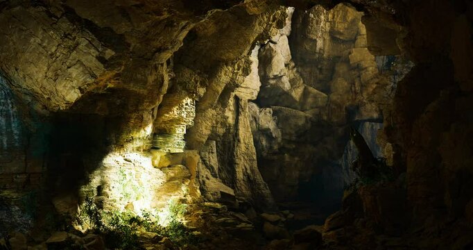 Exploring a vast underground cave filled with rock formations and illuminated patches of light. The atmosphere is damp and earthy, enhancing the sense of adventure and discovery.
