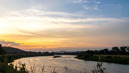 River flowing towards a golden sunset, framed by hills and trees