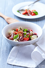 Simple salad with cherry tomatoes, feta cheese, kalamata olives, red pepper and fresh herbs. Bright wooden background. Close up.	