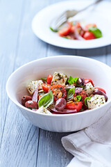 Simple salad with cherry tomatoes, red onion and fresh herbs. Bright wooden background. Close up.	