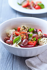 Simple salad with cherry tomatoes, red onion and fresh herbs. Bright wooden background. Close up.	