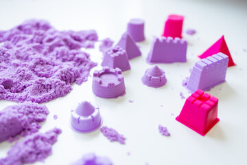Purple kinetic sand with castle molds on white surface