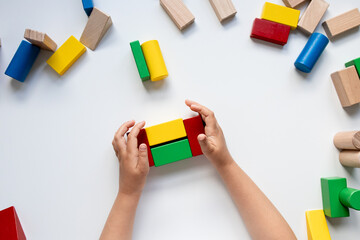 Child hands building with colorful wooden blocks on a white surface