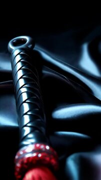 Leather flogger with red tassels on draped black satin, fetish item for suggestive backgrounds.
