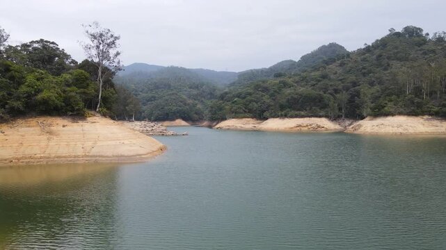 Shing Mun Reservoir with calm water surrounded by mountainous forests and cloudy sky in Hong Kong