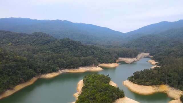 Shing Mun Reservoir with calm water surrounded by mountainous forests and cloudy sky in Hong Kong