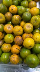 The image captures a large pile of oranges, displaying a mix of green and yellow-orange hues, suggesting varying stages of ripeness or different varieties