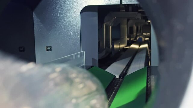 Conveyor moving plastic bottle through machine that inspects materials for recyclable content, crucial for waste separation and environmental protection
