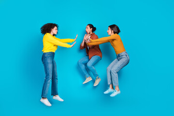 Fototapeta premium Three young friends jumping together vibrant casual fashion against blue background showing joyful gestures of excitement