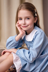 A close-up portrait of a lovely girl with long blond hair against a fabric background. She is...