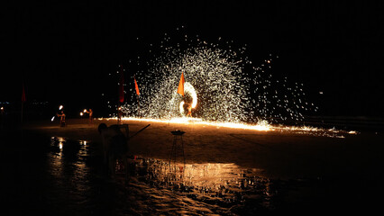 Fire dancers captivating audiences on a beach at night. Creating dazzling showers of sparks with their burning ropes. Vibrant flames illuminating the dark shoreline. Enhancing the tropical atmosphere